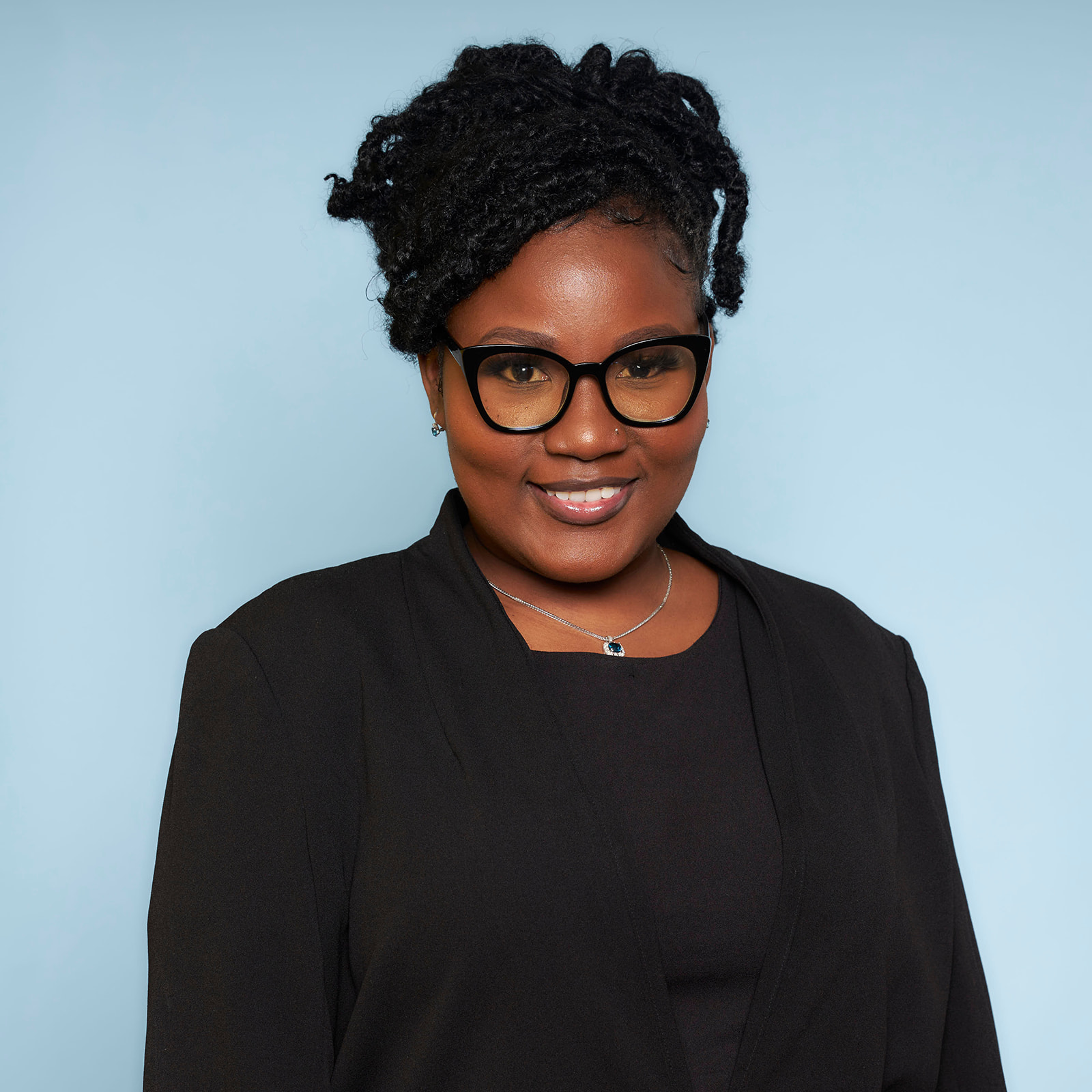 Headshot of a woman in solid black with glasses on a light blue backdrop