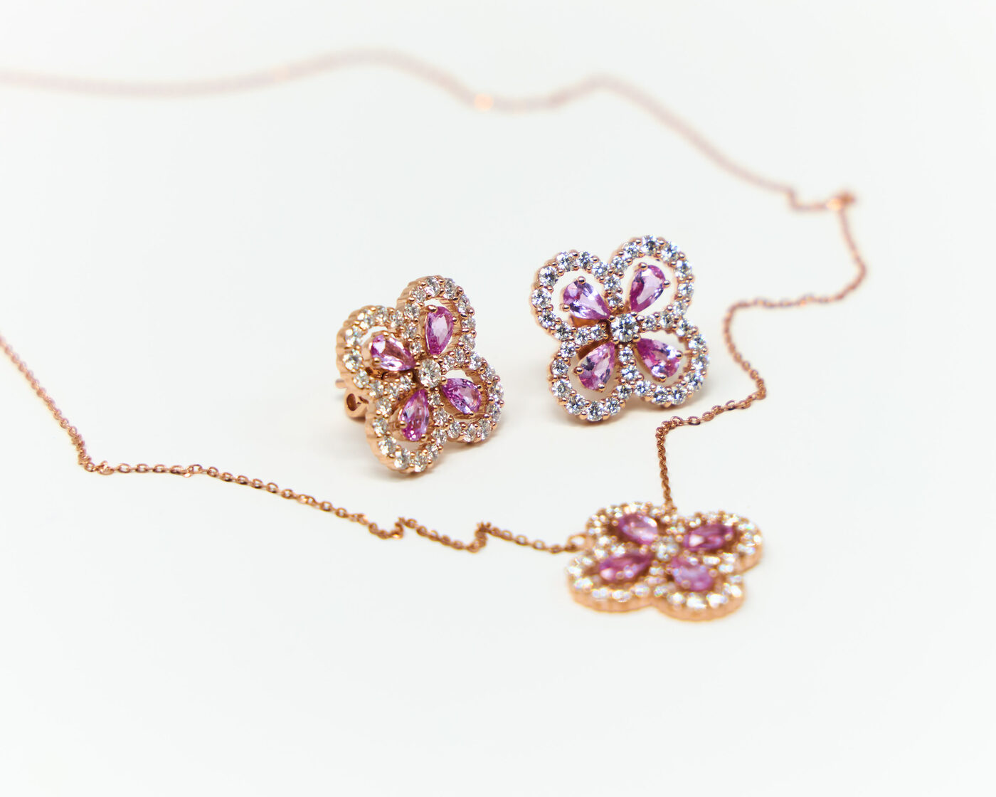 Pink sapphire and diamond clover earrings with a rose gold necklace, jewelry product photography