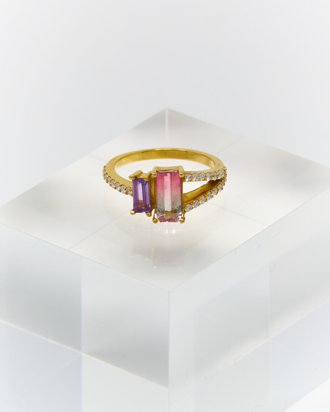Gold ring with bi-color tourmaline, amethyst, and diamonds on an acrylic display