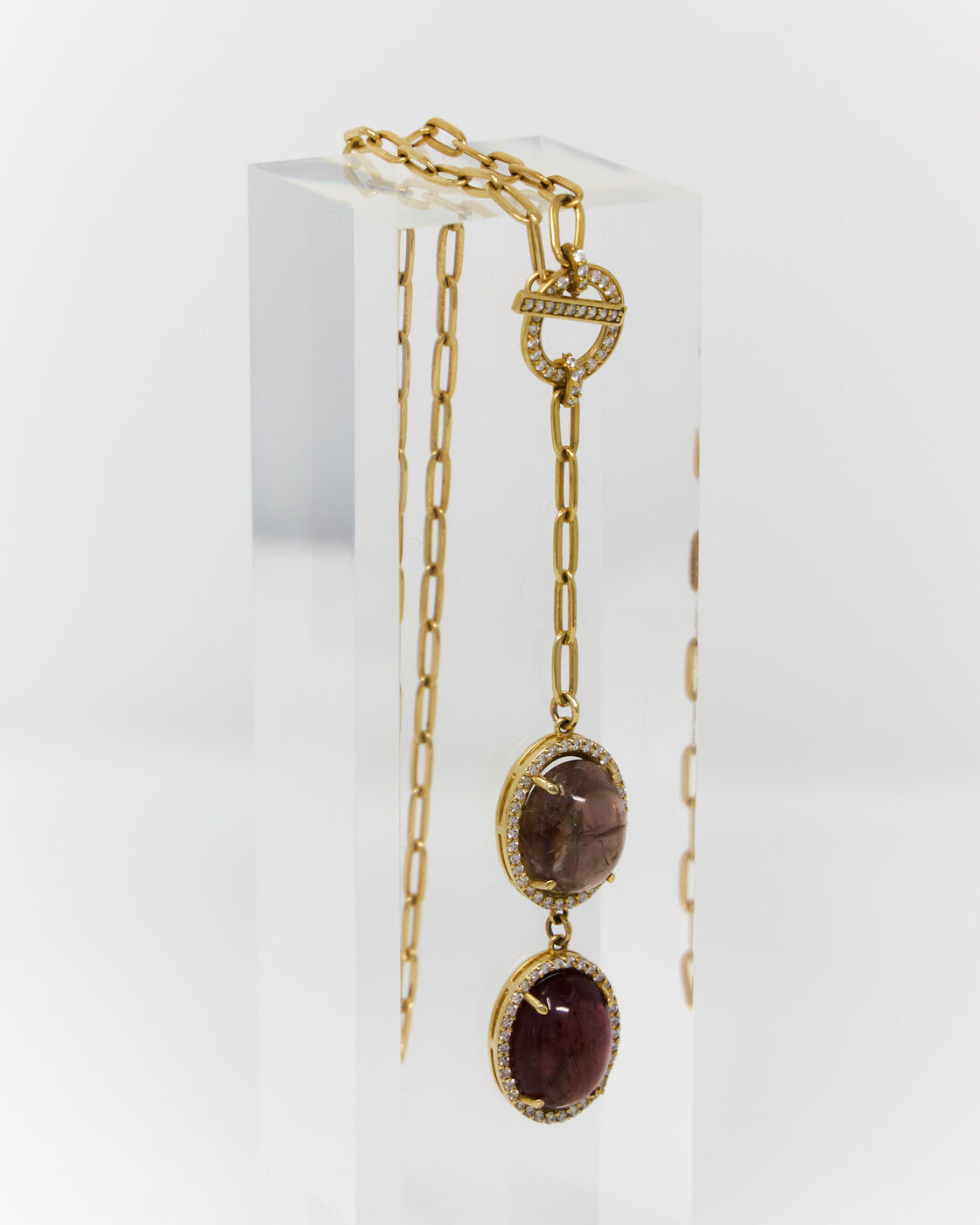 Gold paperclip chain necklace with two tourmaline cabochon pendants on an acrylic stand