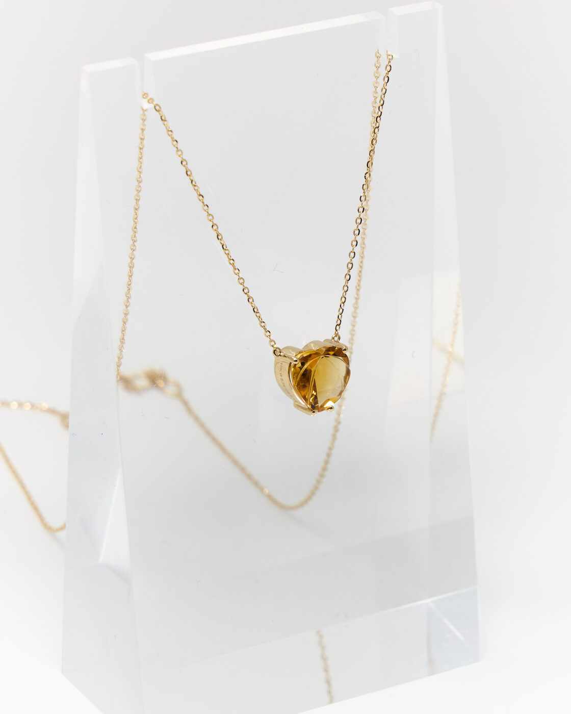 Citrine heart pendant on a fine gold chain, styled on an acrylic stand