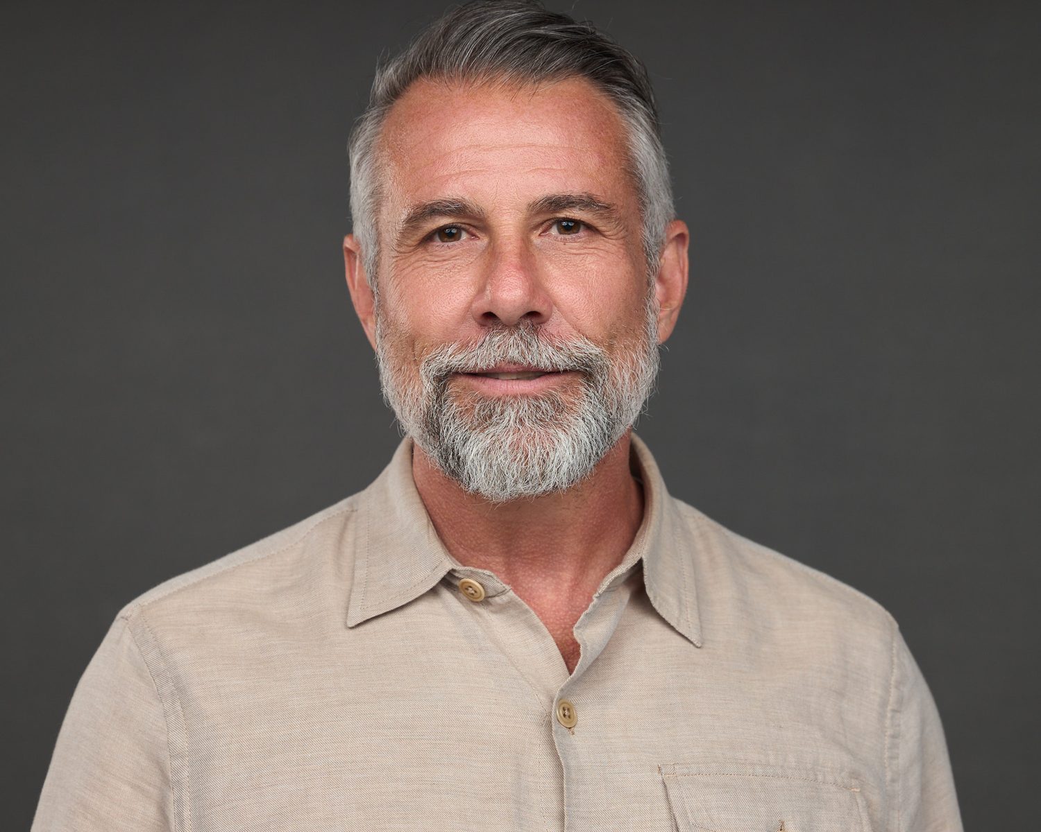 Corporate headshot of a senior executive on a dark grey background